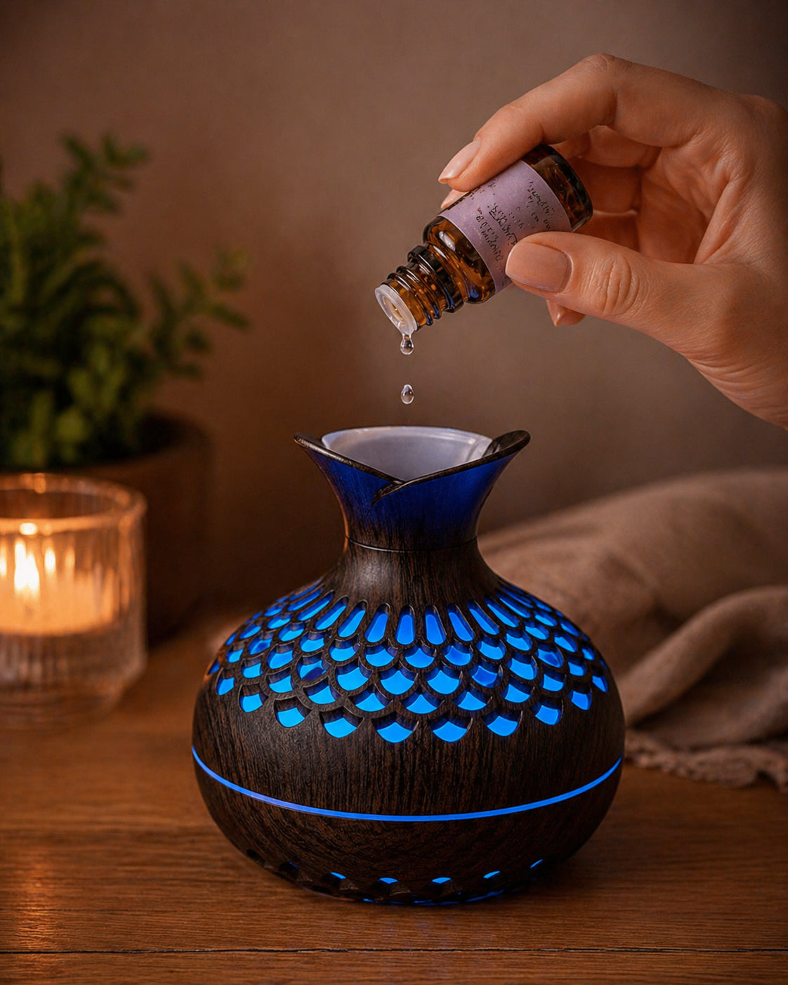 Main féminine ajoutant des gouttes d'huile essentielle dans le diffuseur Someira, ambiance soir